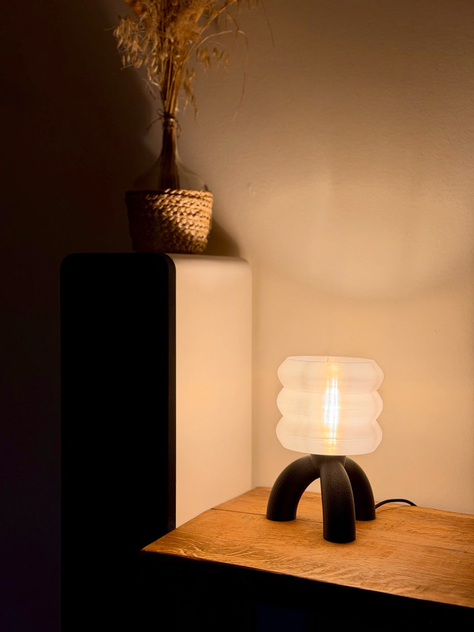 Originalfoto der leuchtenden NIDO mit hellem Ringschirm und schwarzem Strukturfuß auf einem Holzsideboard.